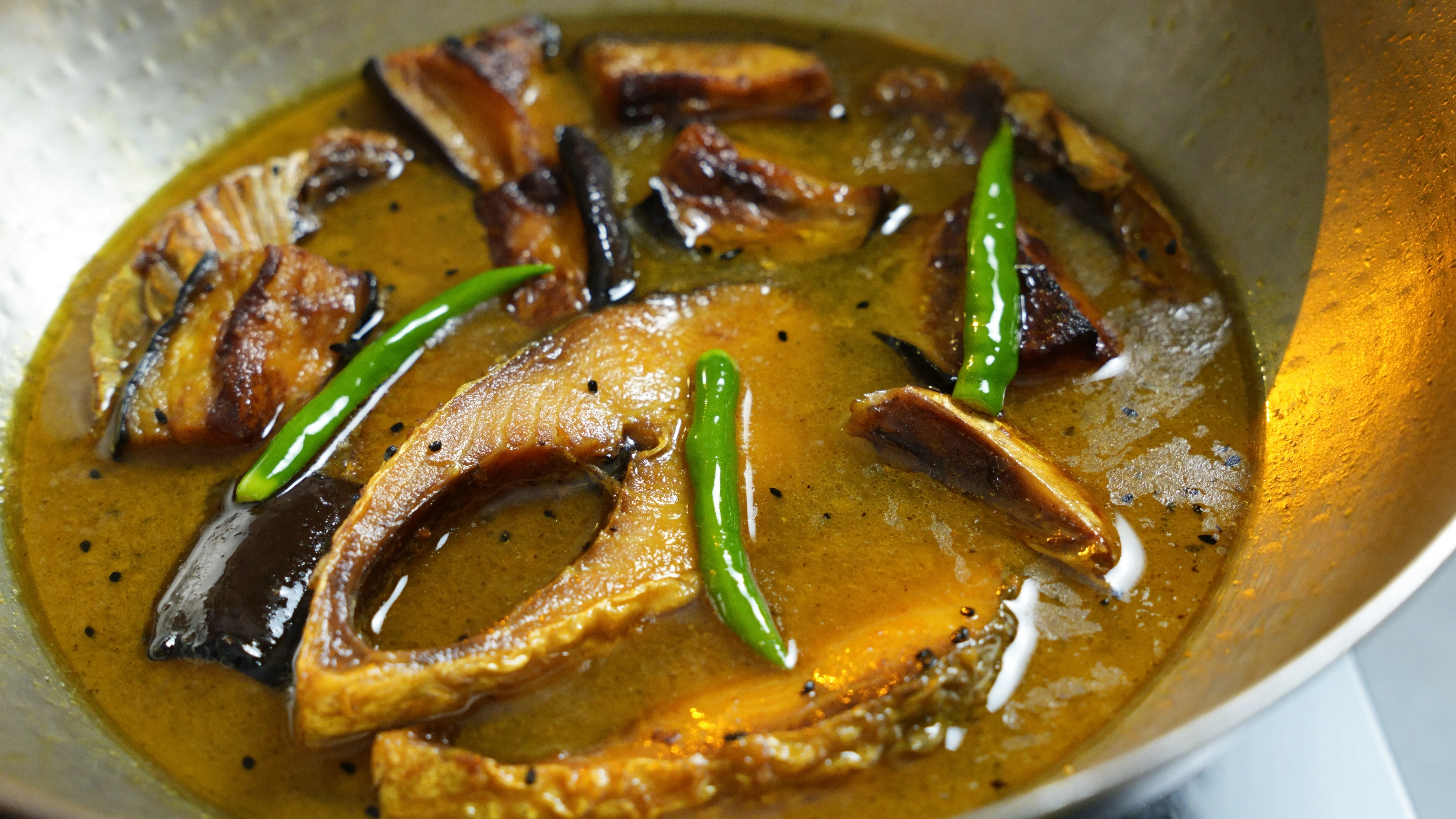 Traditional Bengali Ilish Begun Jhol with hilsa and brinjal in a light turmeric broth.