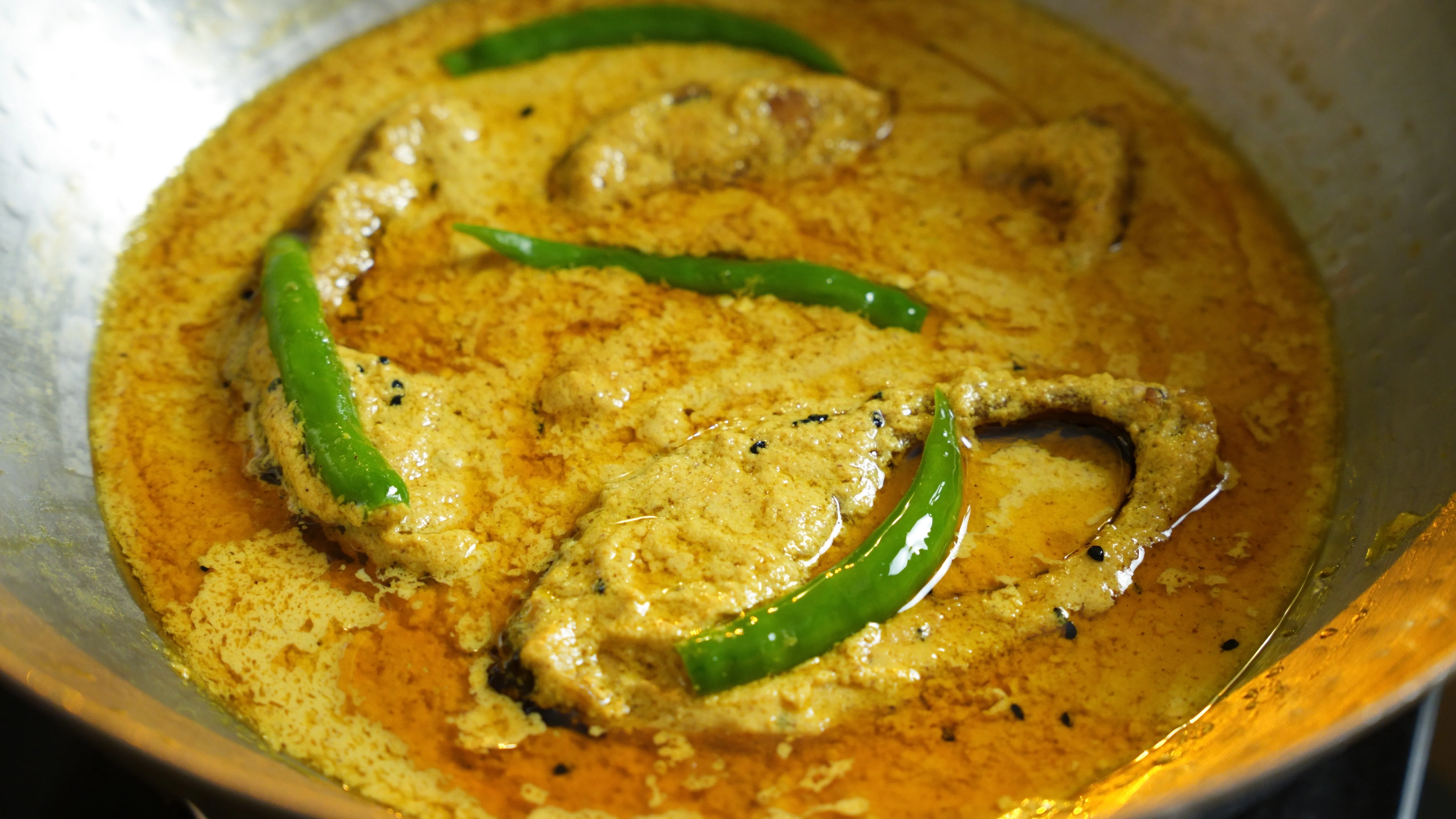 Pieces of hilsa fish in a pale yellow mustard gravy.